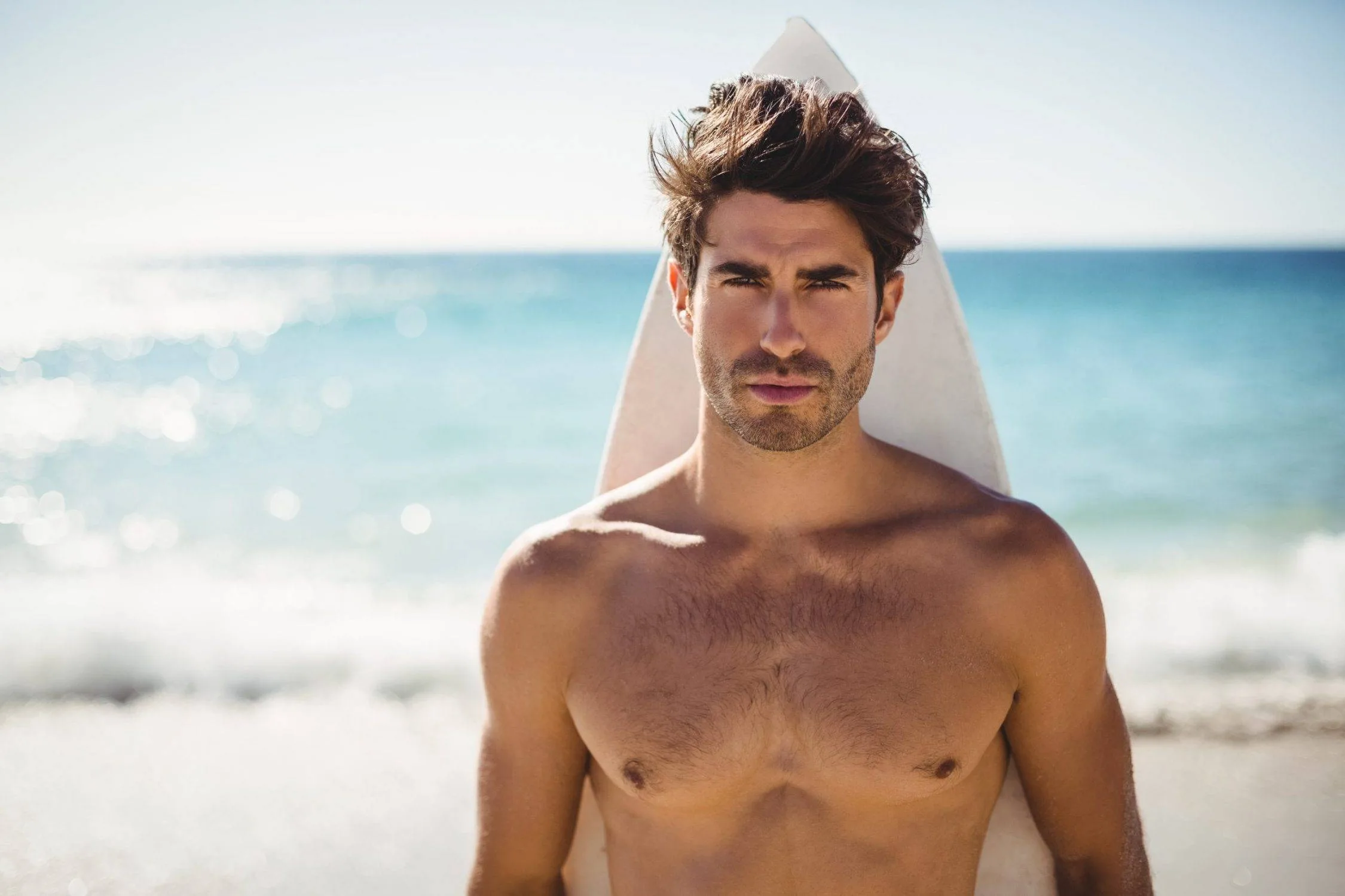 Young Fit Man Posing With Surfboard At The Beach