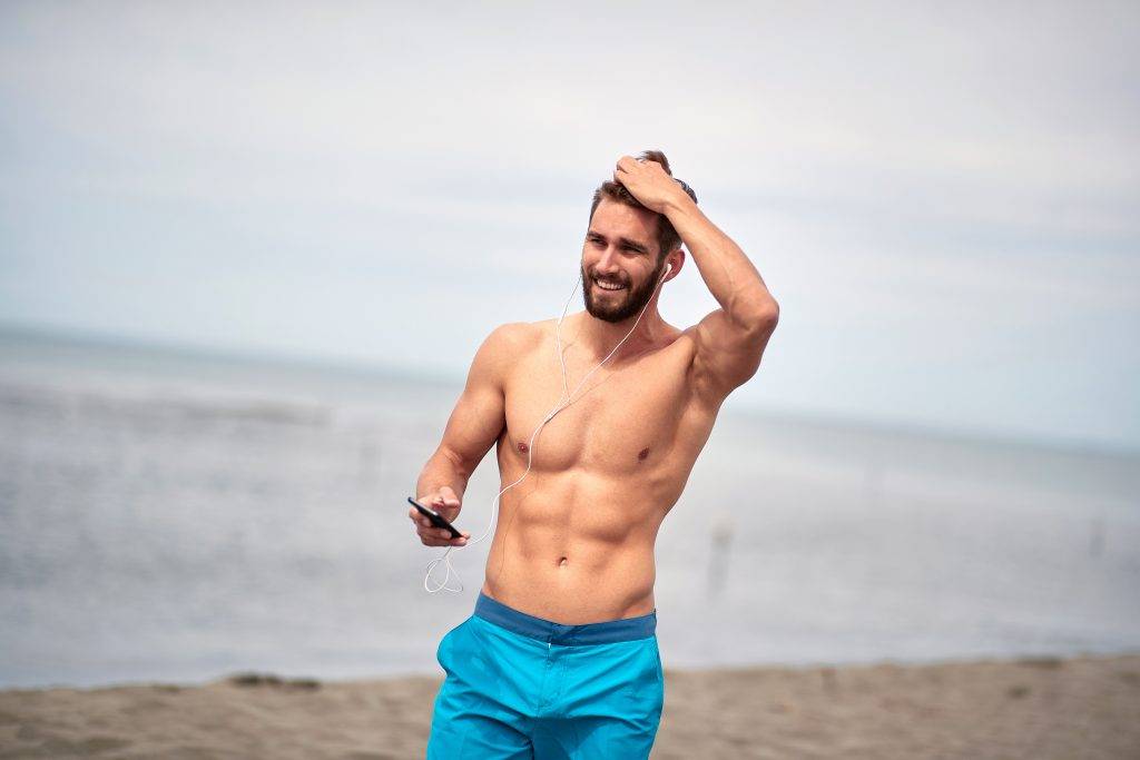 Sexy man listening to music at the beach with a cell phone in his hands